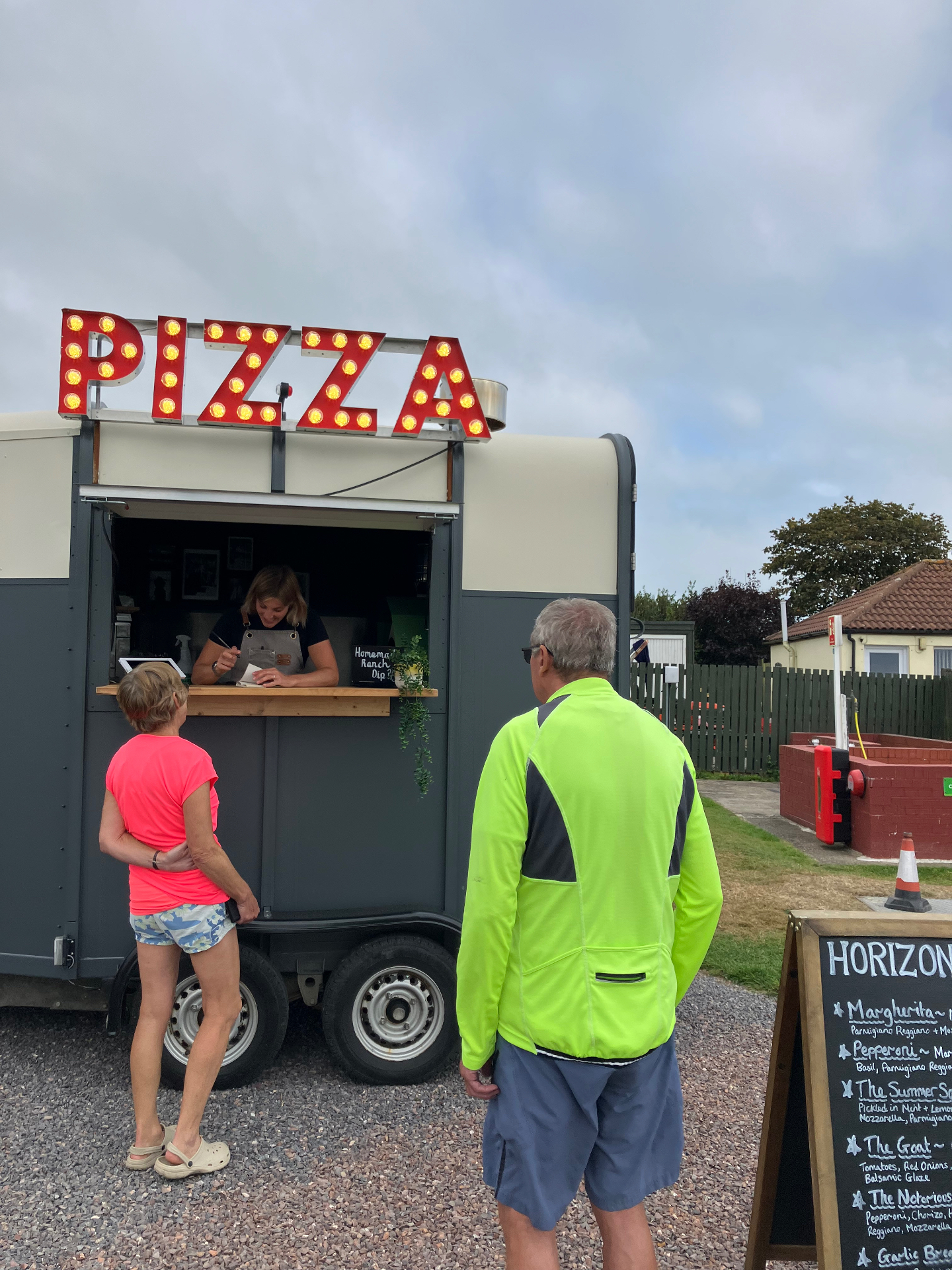 The Horizon Pizza trailer with its lit-up PIZZA sign as customers order at the counter